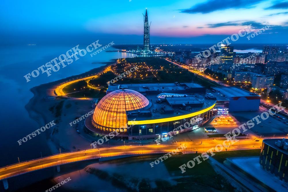 Панорамная фотография Санкт-Петербурга с высоты птичьего полета, на которой запечатлены река Нева, Финский залив, мосты и улицы города. Съемка с дрона позволяет увидеть масштаб городской инфраструктуры, красоту набережных и архитектурные ансамбли Северной столицы России. Фотография передает атмосферу современного и исторического Петербурга, гармоничное сочетание водных пространств и городской архитектуры. Панорамный вид раскрывает величие мостов, перспективу улиц и уникальные пейзажи города на Неве. Снимок идеально подходит для туристических публикаций, фотостоков, рекламы, оформления интерьеров и материалов о достопримечательностях Санкт-Петербурга.